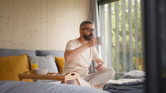 Mature man having breakfast and working in tiny house, in front of nature. Freelancer office concept