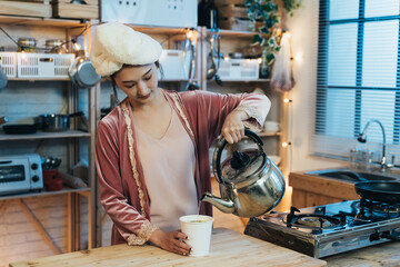 portrait hungry asian woman with towel on head is pouring hot water from kettle into the cup while...