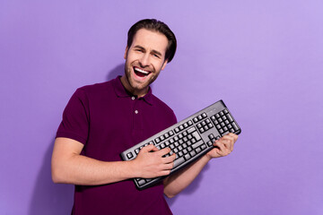 Photo of cool millennial brunet guy hold keyboard wear violet t-shirt isolated on purple color background