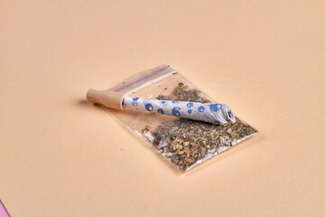 Close-up joint and packet of weed isolated on beige background. Marijuana smoking accessories.