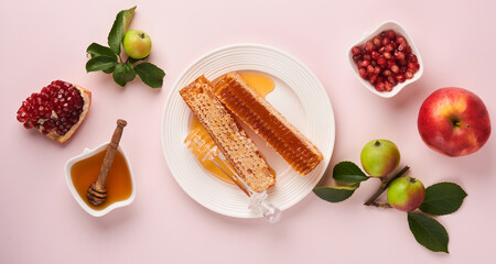 Rosh Hashanah. Honey jar, honeycomb, apple and pomegranate on simple pink background. Jewish New Year holiday greeting card. Rosh Hashanah holiday attributes. Banner.