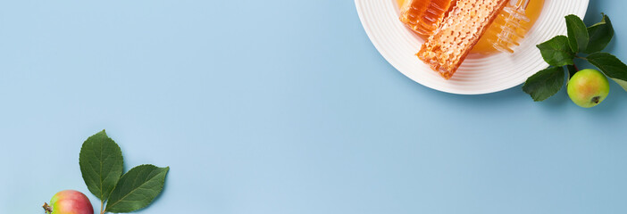 Rosh Hashanah. Honey jar, honeycomb, apple and pomegranate on simple blue background. Jewish New Year holiday greeting card. Rosh Hashanah holiday attributes. Banner.