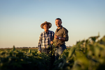 Portrait of two farmers in a field examining soy crop at sunset.