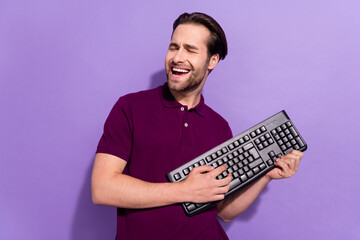 Photo of funky young brunet guy play keyboard wear violet t-shirt isolated on purple color...