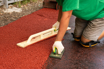 Workers cover the rubber coating on the playground. Soft covering. The process of leveling crumb...