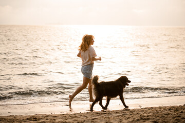 beautiful view on woman running along sandy beach at water with her dog