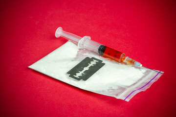 Close-up filled syringe with razor on pack of white cocaine. Drug use and addiction concept.