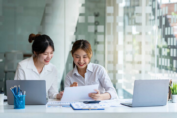 Obraz premium Two young female accountants in casual clothes working with laptops and discussing company investment results and profits and annual bonuses, finance ideas, and collaboration.