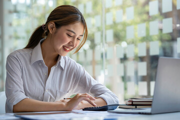 Obraz premium crop shot of business woman checks her work and uses a calculator to calculate her annual financial statements. Turnover and Profit Balance Sheet Making financial records in paper audits.
