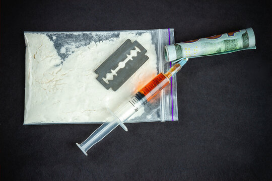 Top View Accessories For Drug Use On Black Background. Syringe With Razor And Snorting Tube Made Of Money.