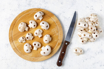 Cutting board with fresh wild mushrooms in the form of skulls and knife on white table. Edible Halloween Concept