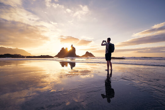 Man during photographing landscape with cliff. Photographer on beach at beautiful sunset. Tenerife, Canary Islands, Spain..