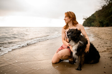 dog with young woman are sitting on the sandy shore of the beach