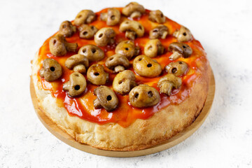 Homemade pizza with tomato sauce and mushrooms in the form of skulls. Concept for Halloween celebrations