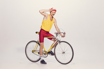 Portrait of young man in colorful clothes, uniform riding bike isolated over grey background....