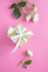 Gift box and white roses on the pink background.Top view. Location vertical.