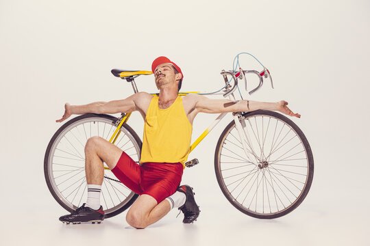 Portrait of young man in colorful clothes, uniform leaning on bike and resting isolated over grey background
