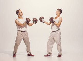 Portrait of two men playing, boxing in gloves isolated over grey studio background. Funny image of...