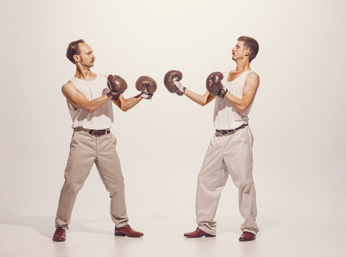 Portrait of two men playing, boxing in gloves isolated over grey studio background. Funny image of two friends