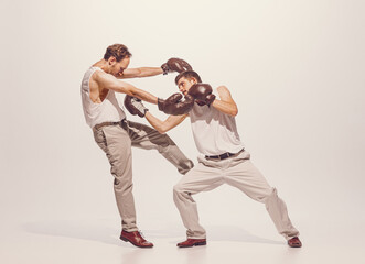Portrait of two men playing, boxing in gloves isolated over grey studio background. Artistic friends