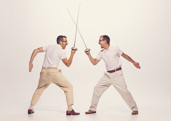 Portrait of two men in a suit fighting with swords isolated over grey studio background. Emotively...