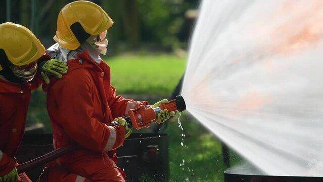In Industry safety fire fighter team  knee down on  training fight with gas and oil fire by hold hose together spray jet turbulence water and foam pushing fire to extinguish remove oxygen
