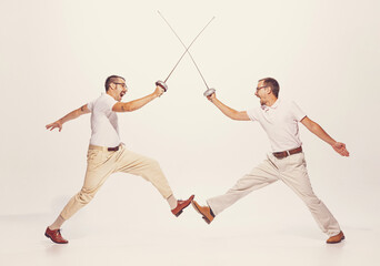 Portrait of two men in a suit fighting with swords isolated over grey studio background. Friends...