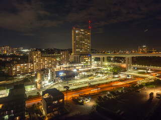 Fototapeta na wymiar Apartment tower rises above Maiko Station and criss-cross roads at night