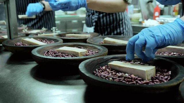 Chef's hands preparing a dish, serving on a bed of beans