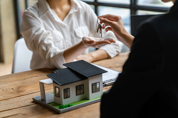 Cropped image of a real estate agent selling broker holds the keys and the model house is given to the customers, home insurance, and Real estate concept.
