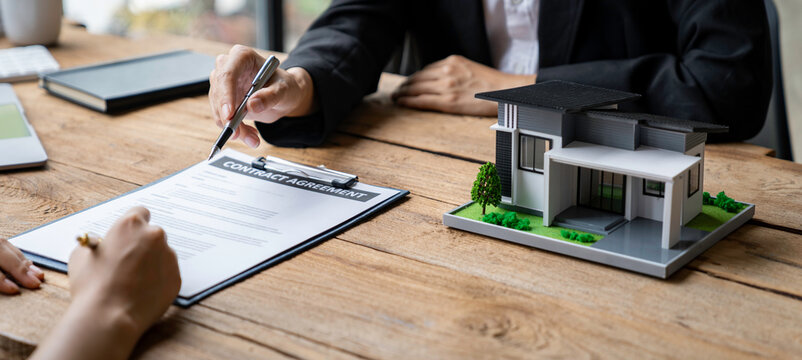 Crop a photo of a real estate agent helping clients read and sign contract documents at their desks with house designs. along with home insurance