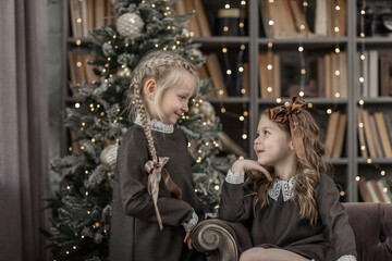 Two cute 5-6-year-old girls in a room with bookshelves in New Year and Christmas decorations. Retro...