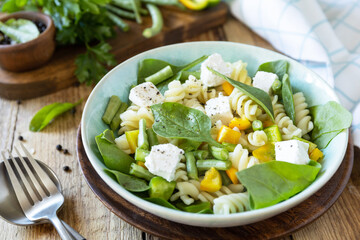 Cold delicious pasta salad, italian cuisine. Whole wheat fusilli pasta with  feta, green bean and pepper on a wooden background.