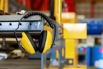 Yellow protective earmuffs hang on heavy industrial machines. This concept is a PPE device.