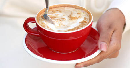 Cup of creamy cappuccino coffee in female hands. Woman holds portion of hot aromatic drink with froth. 