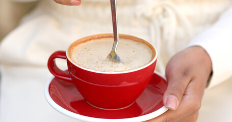 Cup of creamy cappuccino coffee in female hands. Woman holds portion of hot aromatic drink with froth. 