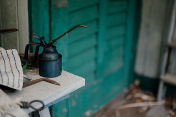 Old oil can sitting on a white table in front of a teal door of a workshop