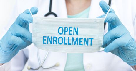Open enrollment text on a protective blue mask in the hands of a doctor, medical concept