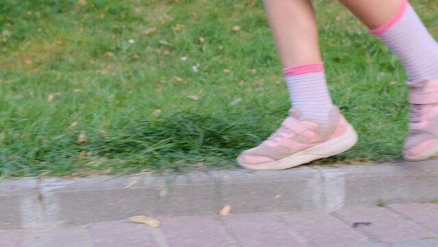children's feet walk on the sidewalk on the street, a schoolgirl walks down the street in good weather. Close-up