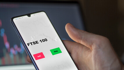 An investor's analyzing the FTSE 100 etf fund on screen. A phone shows the ETF's prices London England london ftse england to invest