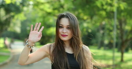 Pretty girl waving hello and inviting to come with hand and finger outdoors