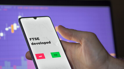 Un investisseur analyse le fonds ETF développé par FTSE à l'écran. Un téléphone affiche les prix de l'ETF Londres Angleterre Londres ftse Angleterre pour investir, texte en anglais.