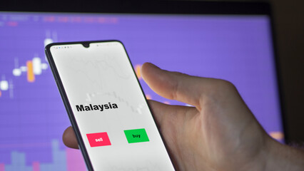 Un investisseur analyse le fonds ETF malaisien à l'écran. Un téléphone montre les prix des ETF malaisiens malaisiens malaisiens à investir., texte en anglais.