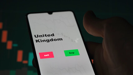 Un investisseur analyse le fonds ETF du Royaume-Uni à l'écran. Un téléphone affiche les prix de l'ETF au Royaume-Uni pour investir, texte en anglais.