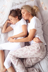 Obraz na płótnie Canvas a woman laying on top of a bed next to a little girl, wearing white pajamas, having a good time, istock, elegant shot, with a white, comfortable, heartwarming, radiant morning light, stock image, full