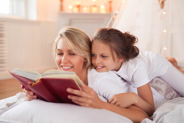 a mother and daughter reading a book on a bed, stock image, in the bedroom at a sleepover, full length shot, istock, photo of a beautiful, reading new book