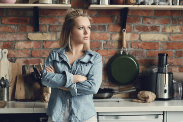 Image of a beautiful woman standing with crossed arms in the kitchen and looking away