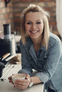 Portrait of a young smiling woman enjoying a cup of coffee in the kitchen at home