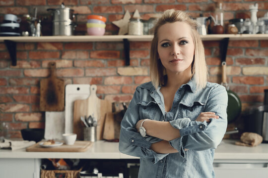 Image of a beautiful woman standing with crossed arms in the kitchen and looking at camera.