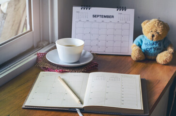 Agenda, planner book, teddy bear,  and cup of coffee placed on office desk. Diary for organizer to...